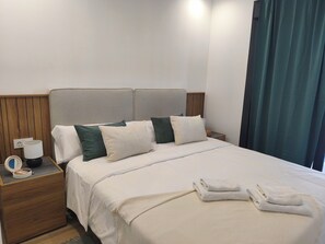 A neatly made bed with a headboard, a bedside table with a lamp and a small decorative item, and a window with curtains. - Lagoons Premium Apartment (Alicante)