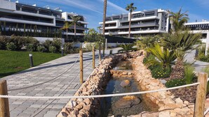 Ein modernes Gebäude mit mehreren Balkonen, einem gepflasterten Weg und einer kleinen Wasserspiele.