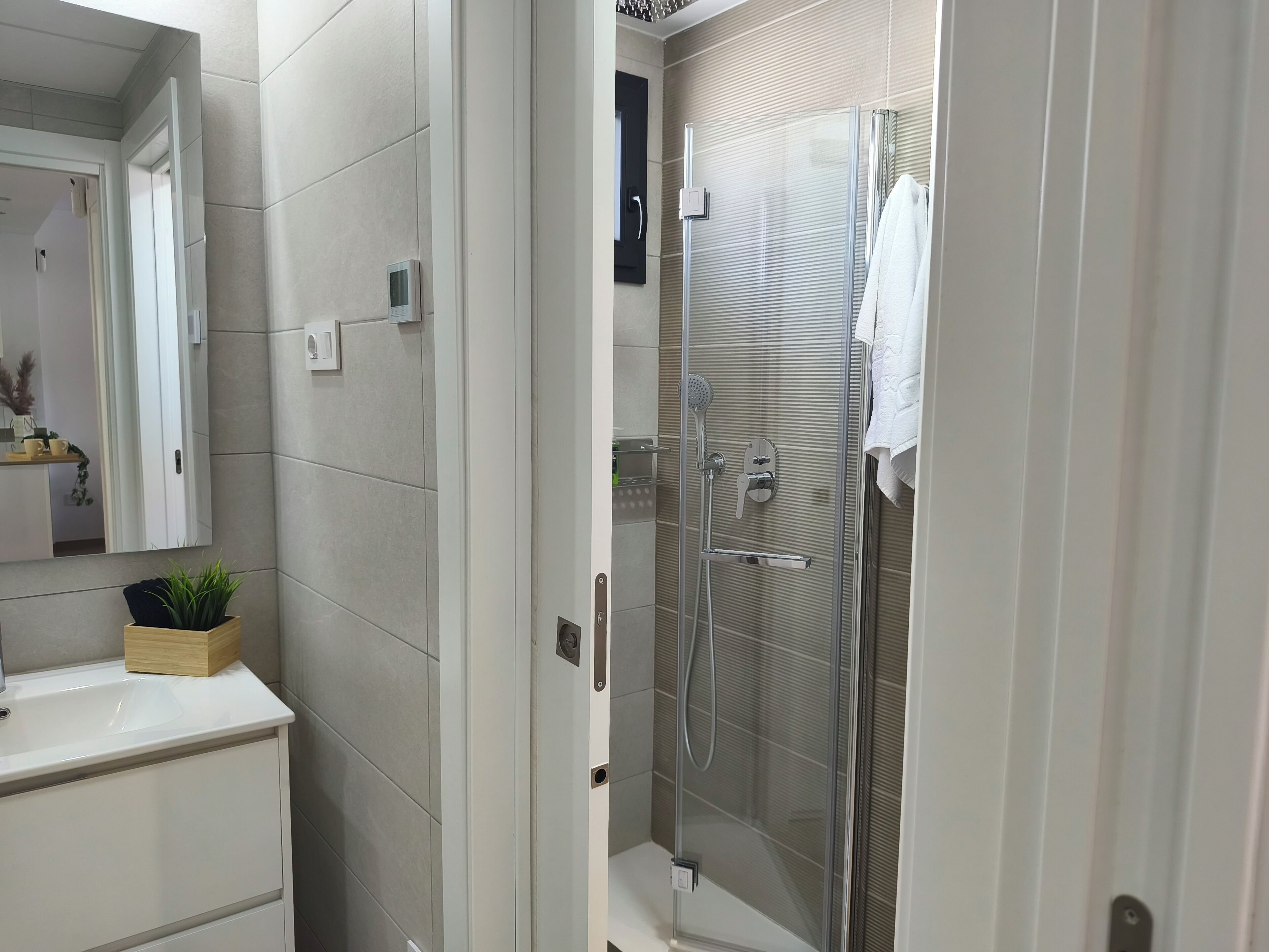 A bathroom with a glass-enclosed shower, a white sink, and a mirror.