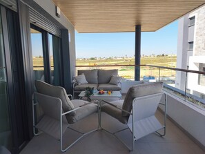 Ein Balkon mit einer Couch, Stühlen und einem Tisch, auf dem sich eine Pflanze und Obst befinden.