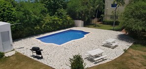 A backyard with a swimming pool, stone patio, and outdoor seating.