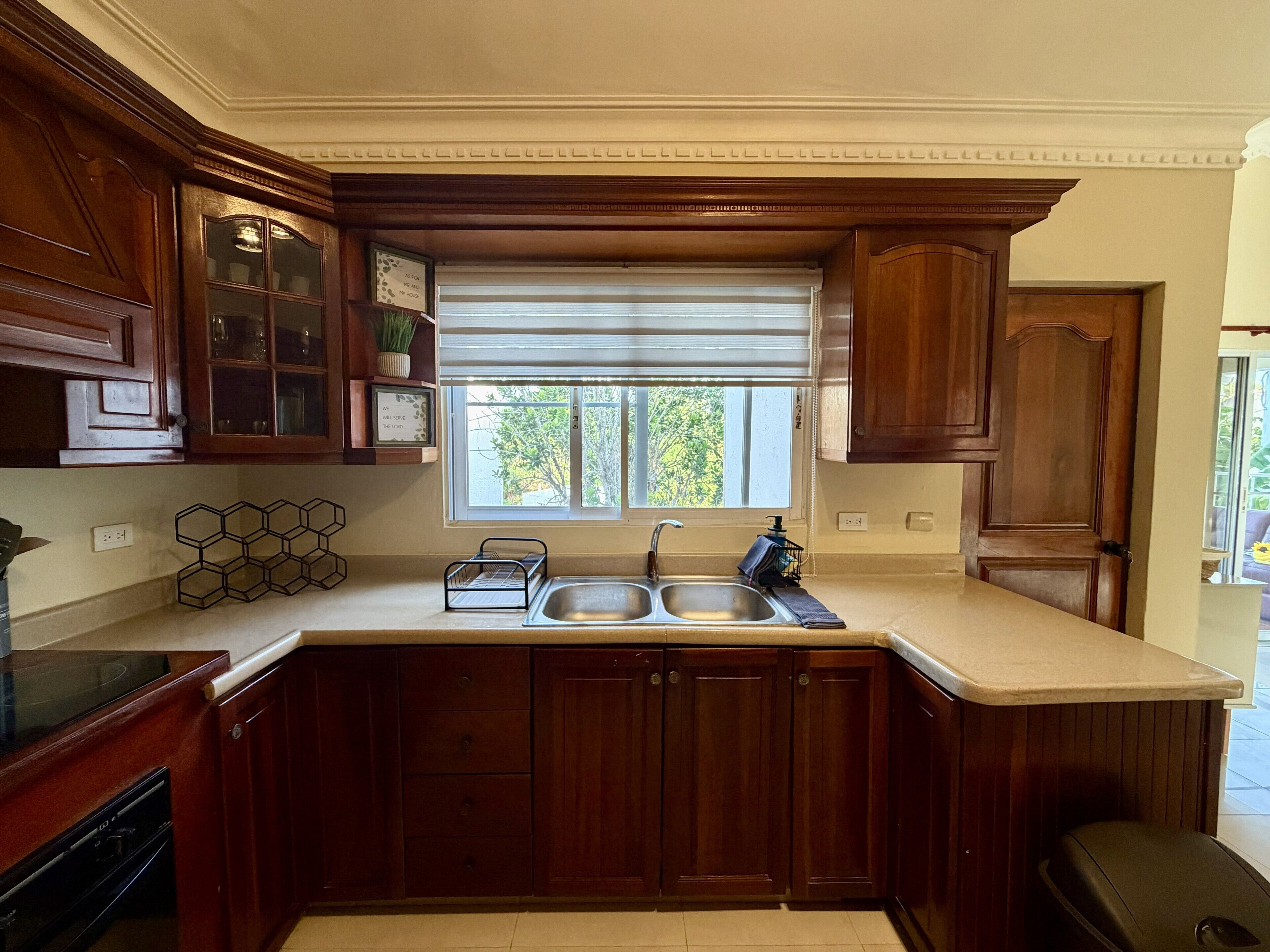 A kitchen with wooden cabinets, a double sink, and a window with blinds.