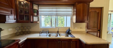 A kitchen with wooden cabinets, a double sink, and a window with blinds.