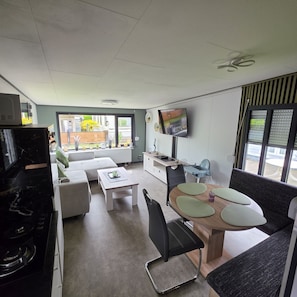 Ein modernes Wohnzimmer mit Sofa, Esstisch, Stühlen, Fernseher und Küchenzeile mit Herd.