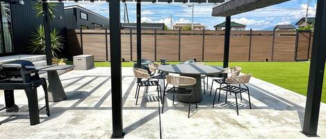 An outdoor patio with a grill, seating, and a pergola structure.