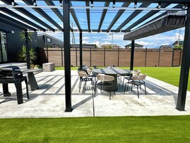 Un patio exterior con una parrilla, asientos y una pérgola.