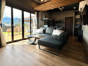 A modern living room with a sofa, a coffee table, and a view of the outdoors through large sliding doors. - Solana Private Villa Minami-Alps (Minami-Alps)