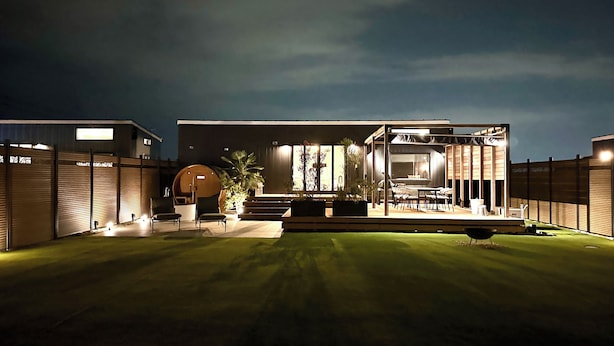 Una casa moderna con un espacio exterior bien iluminado, que incluye una zona de estar y una parrilla.