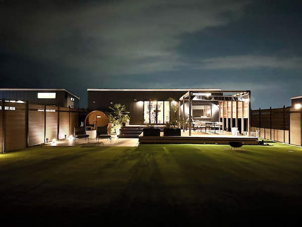 A modern house with a well-lit outdoor area, including a seating area and a barbecue grill.