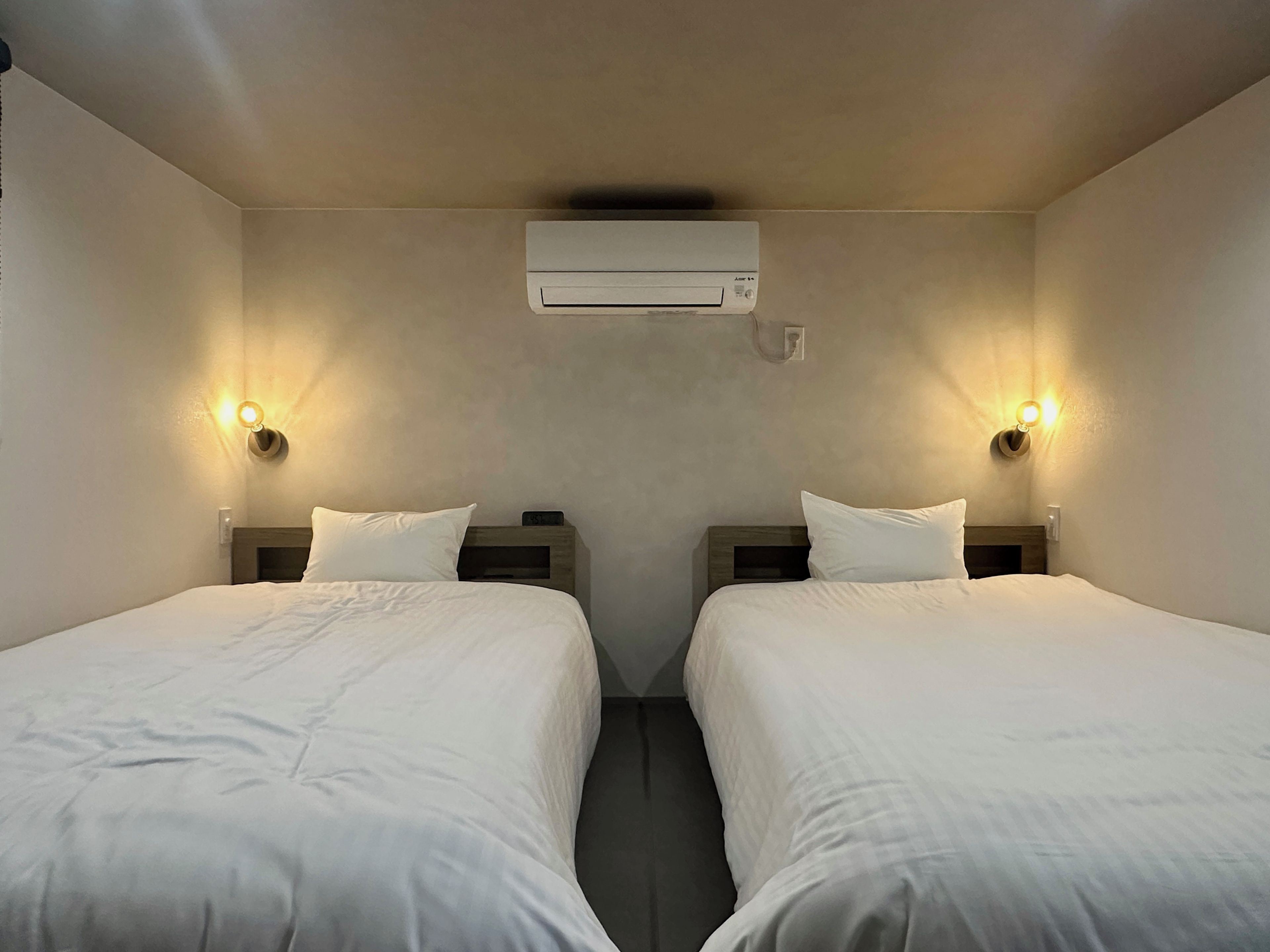 Habitación de hotel con dos camas, aire acondicionado de pared y dos apliques.
