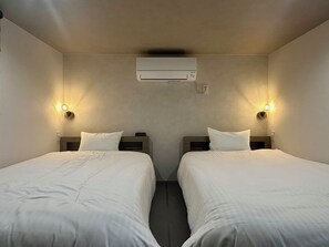 Quarto de hotel com duas camas, ar-condicionado fixado na parede e duas luminárias de parede.