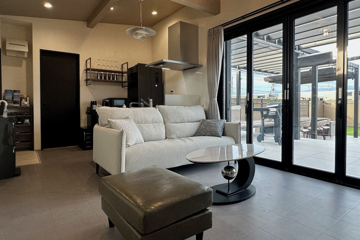 A modern living room with a sofa, ottoman, and a glass coffee table.