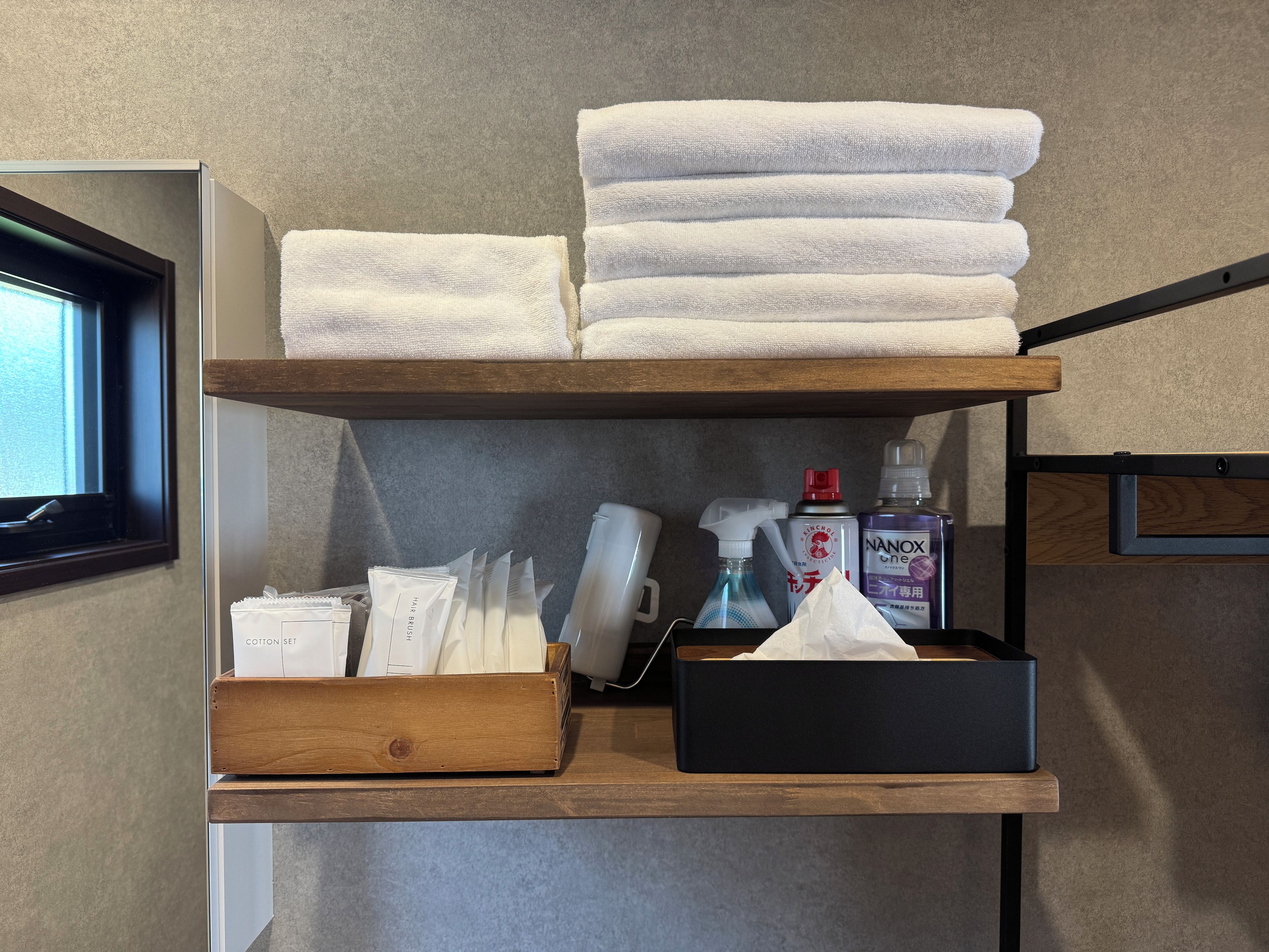 A shelf with neatly stacked white towels, a box of cotton sets, a spray bottle, and a tissue box.
