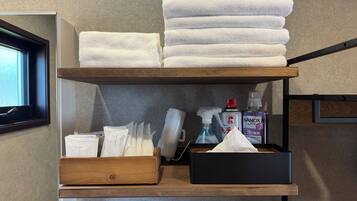A shelf with neatly stacked white towels, a box of cotton sets, a spray bottle, and a tissue box.