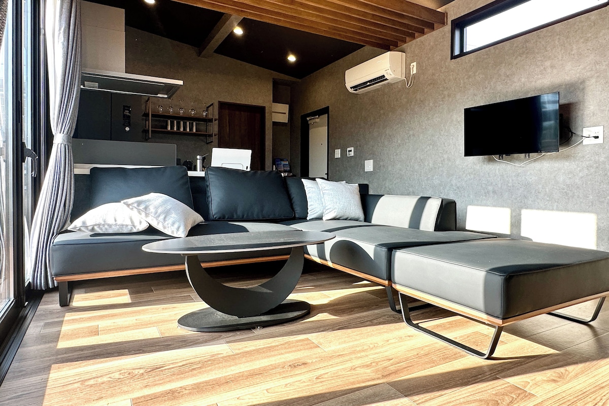 A modern living room with a sectional sofa, a coffee table, and a flat-screen TV mounted on the wall.