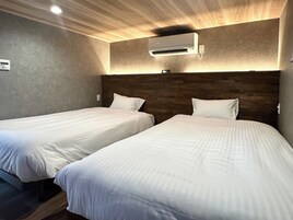 Habitación de hotel con dos camas individuales, cabecero de madera, unidad de aire acondicionado y termostato en la pared.