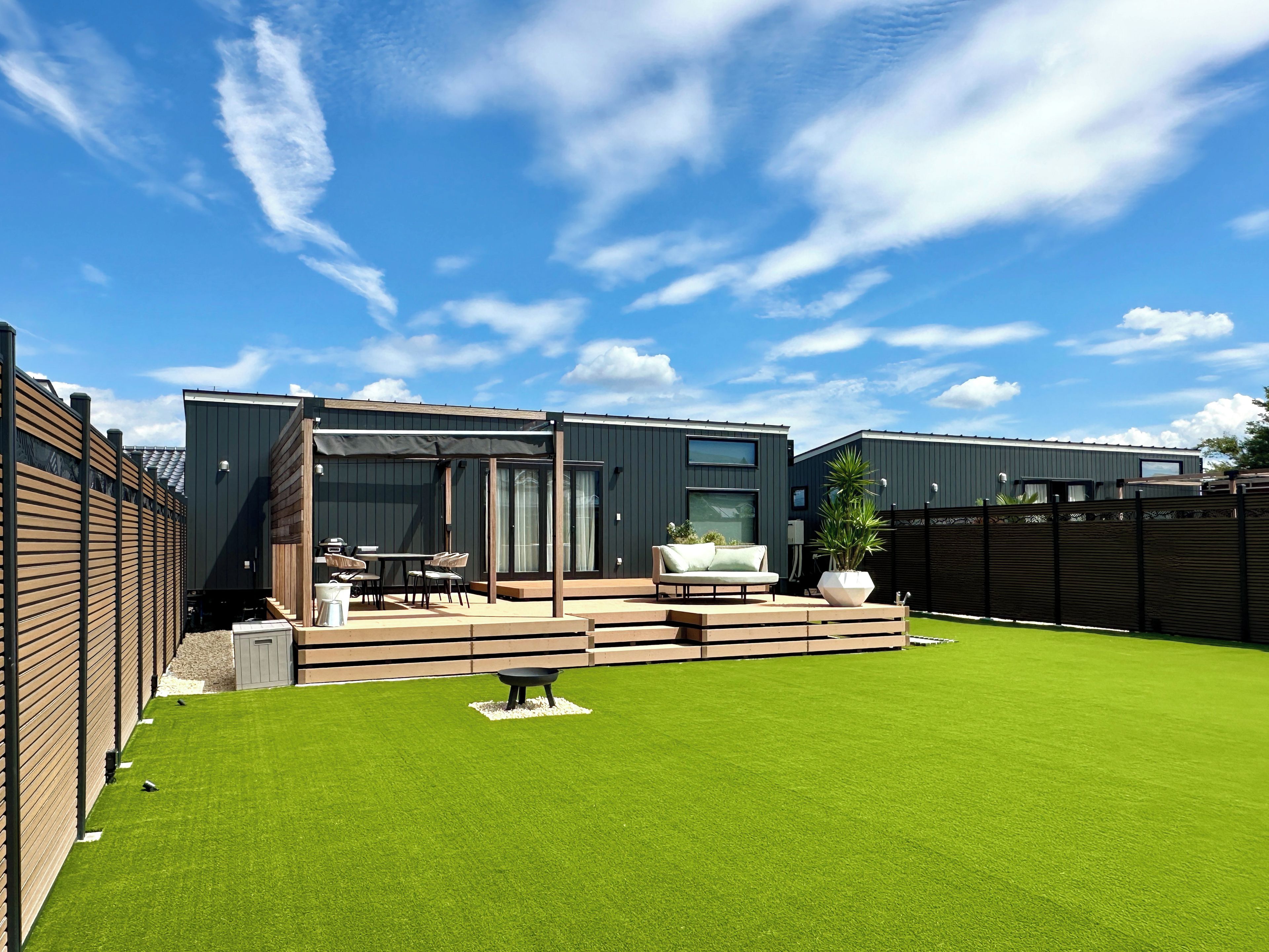 Une terrasse extérieure moderne comprenant un espace repas, un coin salon et une pelouse bien entretenue.