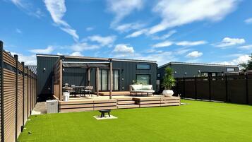 Une terrasse extérieure moderne comprenant un espace repas, un coin salon et une pelouse bien entretenue.