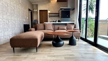 Una sala moderna con un sofá seccional, dos mesas redondas y una cocina al fondo.