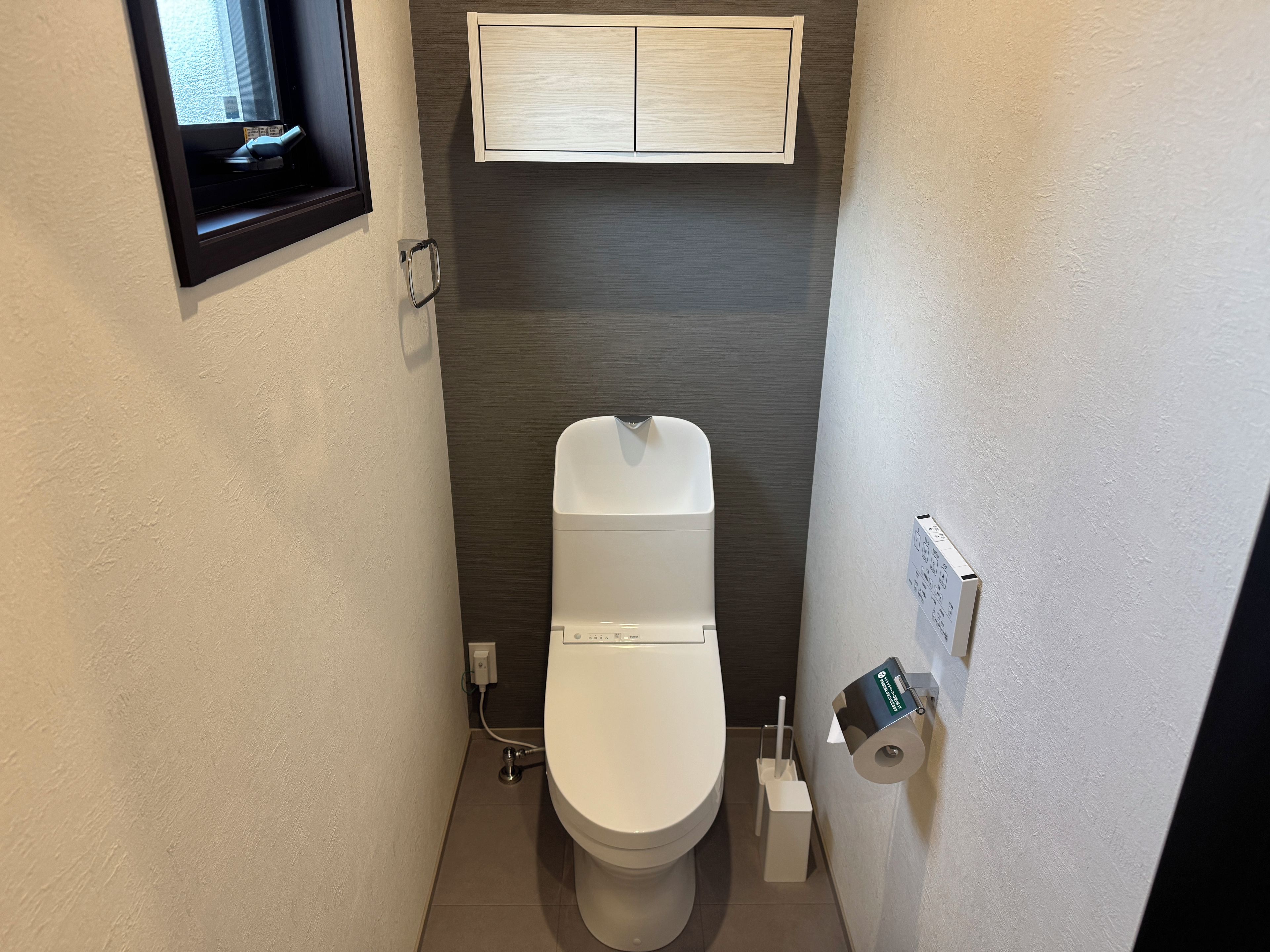 Ein kleines, schmales Badezimmer mit Toilette, einem Händetrockner und einem Papierhandtuchspender.