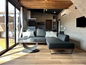 Uma sala de estar moderna com um sofá modular, uma mesa de centro redonda e uma grande porta de vidro deslizante que dá para uma área externa.