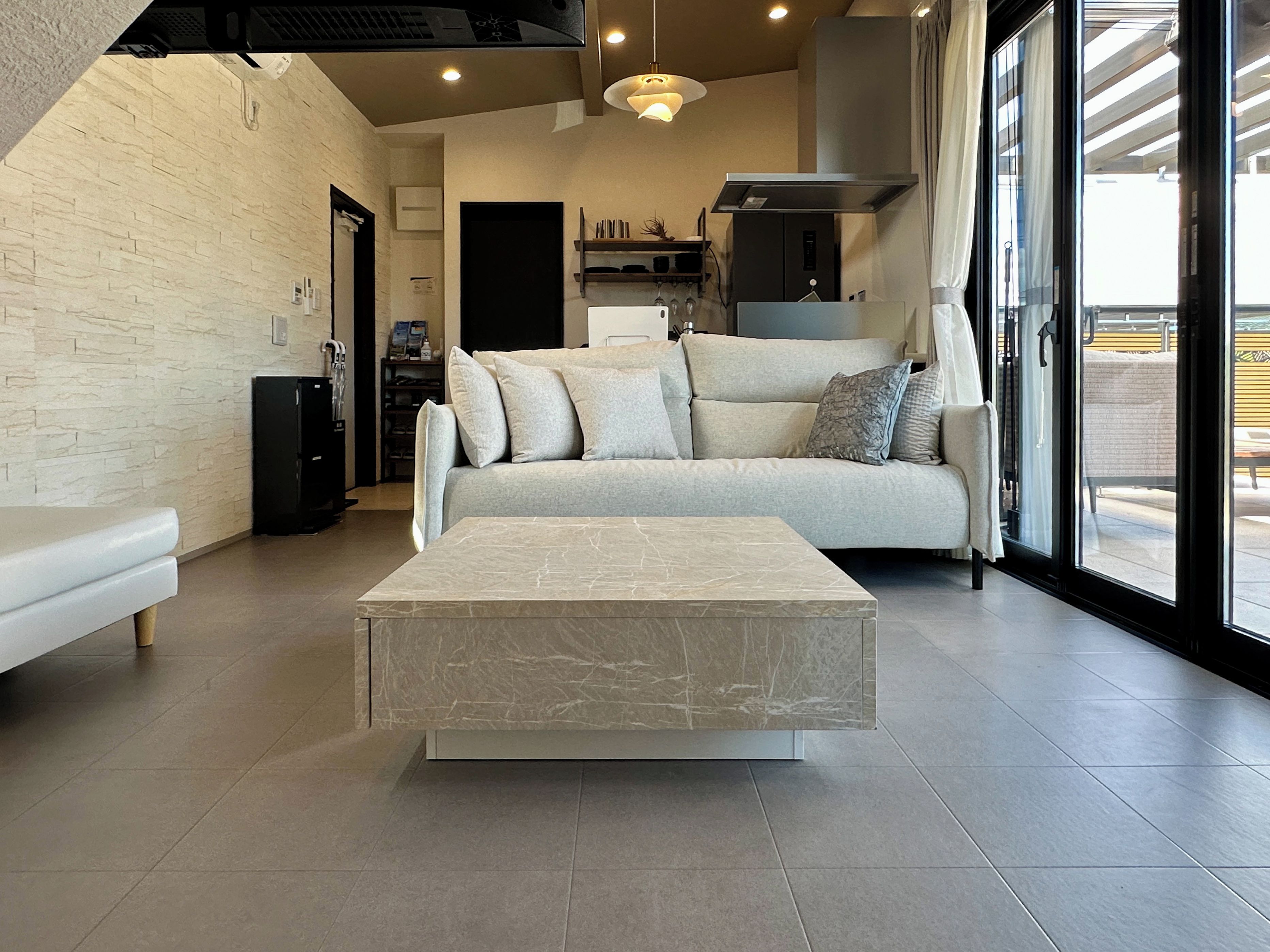 A modern living room with a sofa, a marble coffee table, and a large window offering a view of the outdoors.