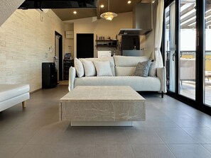 A modern living room with a sofa, a marble coffee table, and a large window offering a view of the outdoors. - Solana Private Villa Minami-Alps (Minami-Alps)