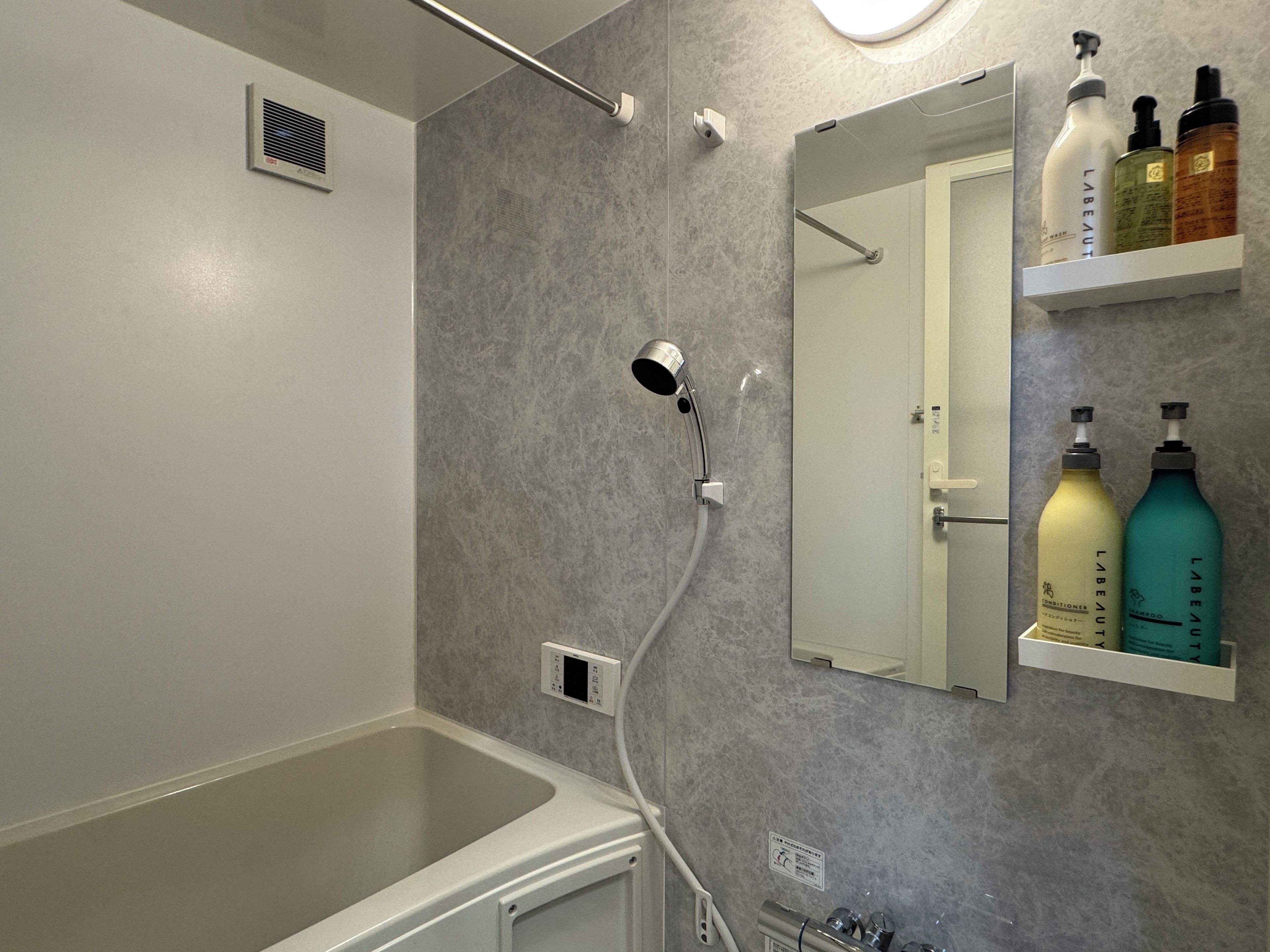 A bathroom with a bathtub, a shower head, a mirror, and a shelf with toiletries.