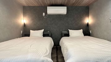 A hotel room with two beds, a wall-mounted air conditioner, and two wall sconces.