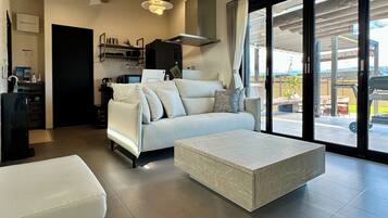 A modern living room with a sofa, a coffee table, and a kitchen area with a stove and cabinets.