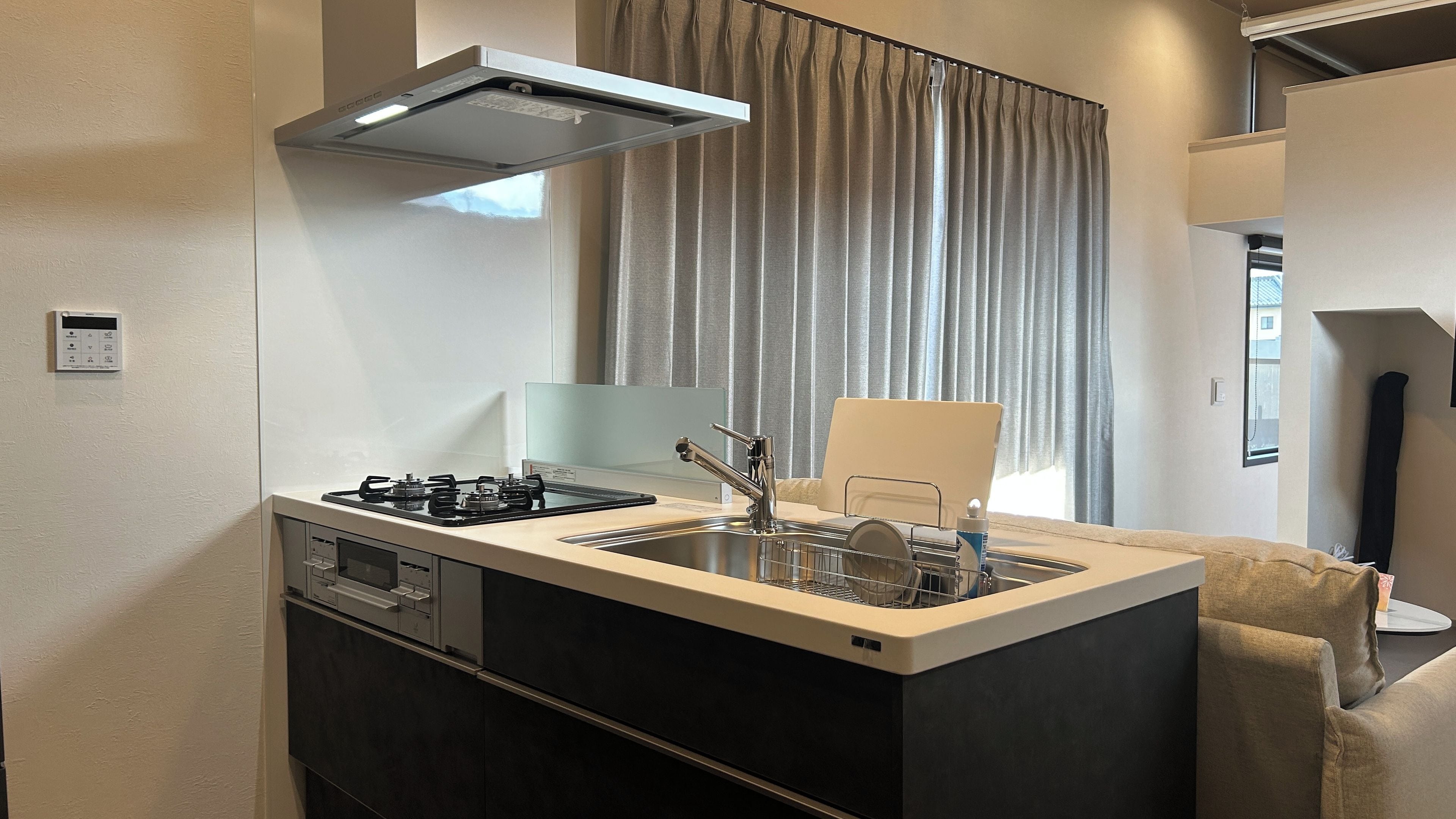 A compact kitchenette with a gas stove, a sink, and a modern range hood.