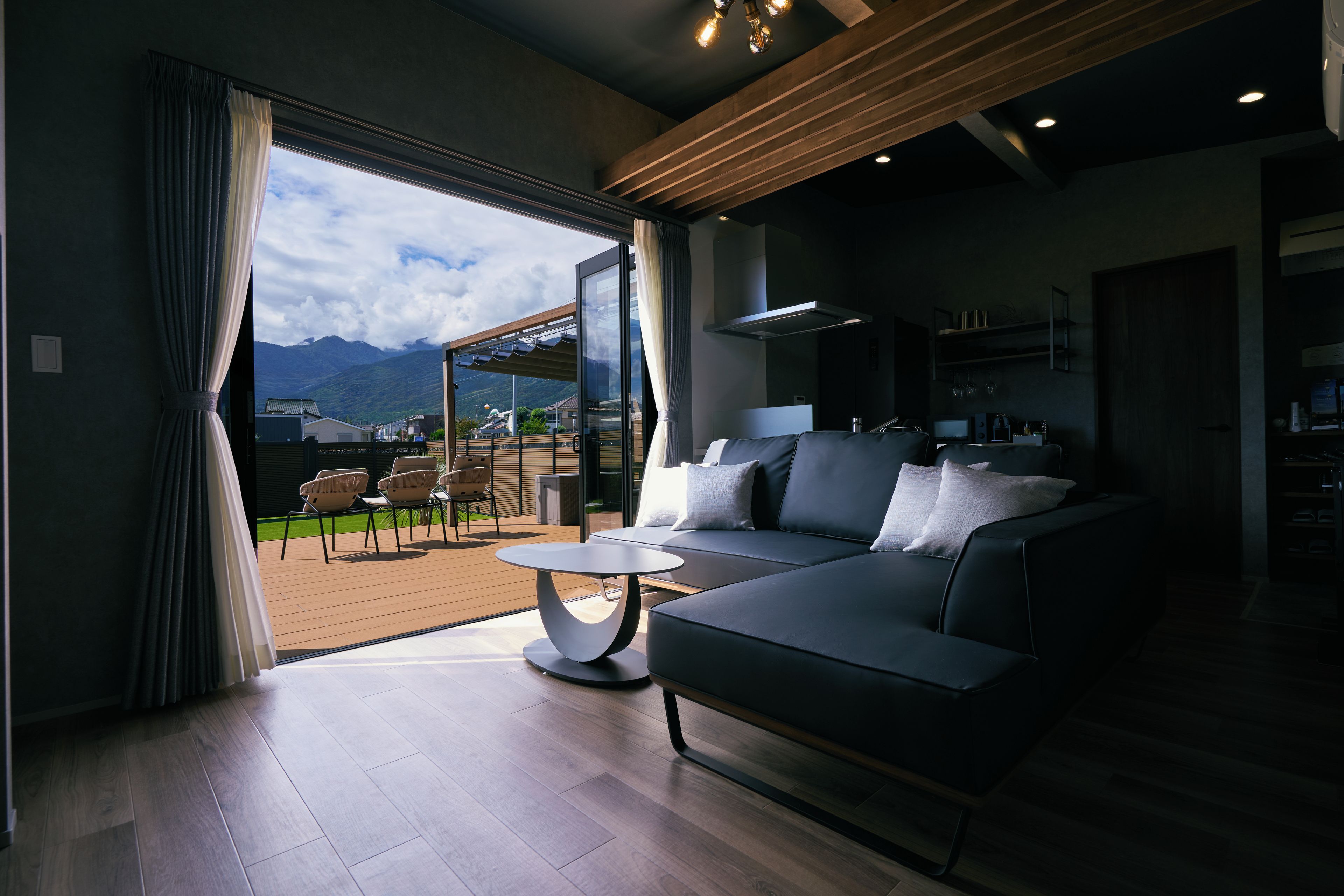 Una sala de estar moderna con un sofá, una mesa de centro y vistas a una terraza y montañas.