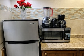 A kitchen with a refrigerator, a microwave, a blender, and a coffee maker.