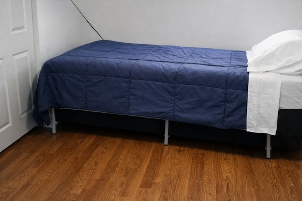 Een eenpersoonsbed met een blauwe deken, witte kussens en een houten vloer.