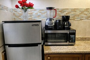A kitchen with a refrigerator, a microwave, a blender, and a coffee maker.