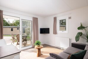 Een moderne woonkamer met een bank, een televisie, een eettafel met stoelen, een schuifpui en een kamerplant.