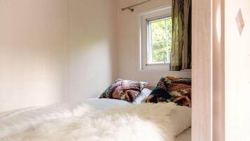 Un dormitorio con cama, ventana con cortinas y vistas al verdor exterior.