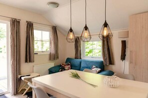 Et moderne køkken med blå sofa, hængende lamper og udsigt til grøn vegetation.