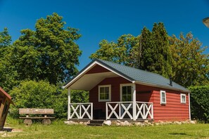 Una baita di legno rossa con un portico, circondata da alberi.