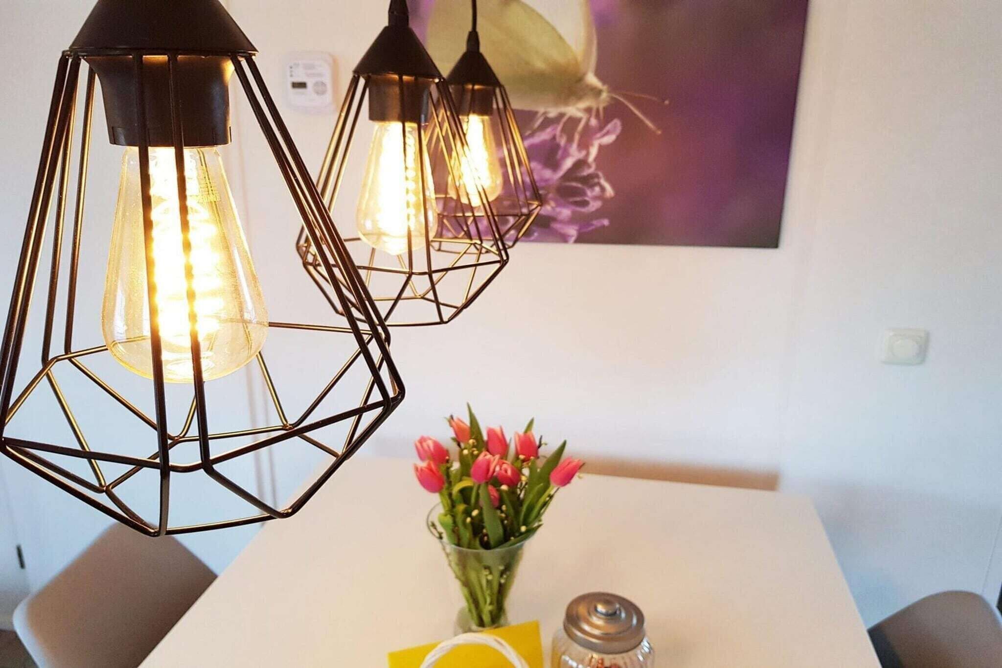 A dining area with a white table, a vase of pink tulips, and three pendant lights with exposed bulbs.