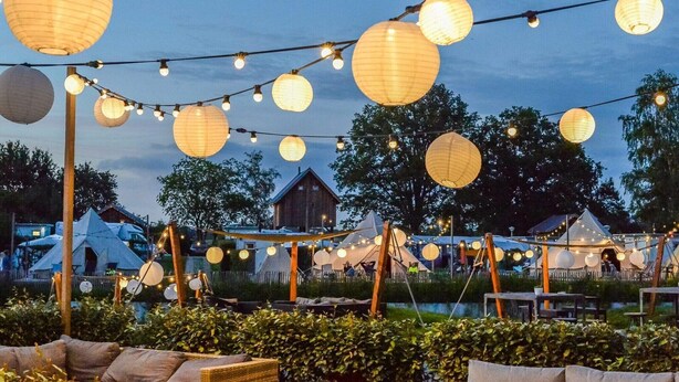 Een camping met tenten, lichtjes en een houten gebouw op de achtergrond.
