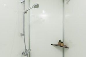 Ducha con cabezal de ducha de mano y grifo instalado en la pared. Se observa un estante pequeño con dos plantas en macetas.