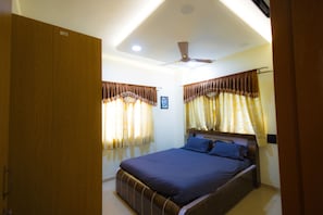 Um quarto com cama, cortinas, ventoinha no teto e guarda-roupa.