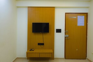 Habitació amb televisió penjada en un panell de fusta, una porta amb un cartell de benvinguda i una petita banca amb un telèfon.