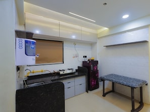 Uma cozinha compacta com um bebedouro, fogão, geladeira e um banco.