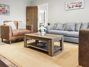 A living room with a brown leather sofa, a grey sofa, a wooden coffee table, and a white vase with flowers.