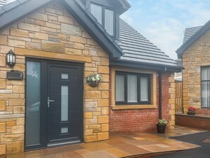 A stone cottage with a black door, a window with a white curtain, and a small garden area. - Barncroft Retreat - UK51692 (High Seaton, near Workington)