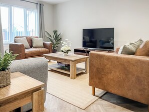 A modern living room with a sofa, coffee table, TV, and a potted plant. - Barncroft Retreat - UK51692 (High Seaton, near Workington)