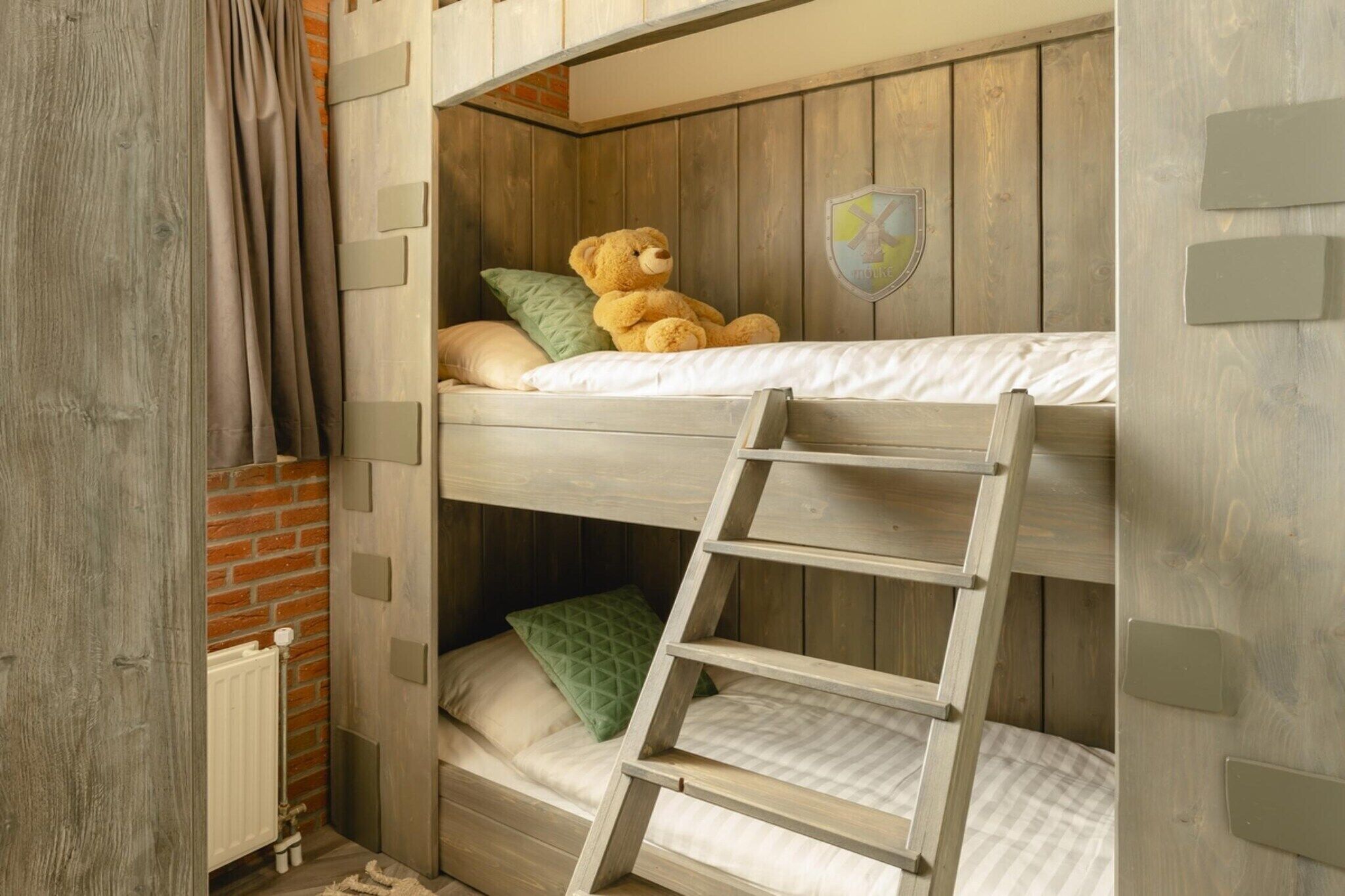 A bunk bed with a teddy bear, a ladder, and a shield emblem on the wall.