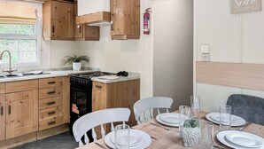 A kitchen with wooden cabinets, a stove, and a dining table set for four with white plates and glasses. - Station House Retreat (Royston)